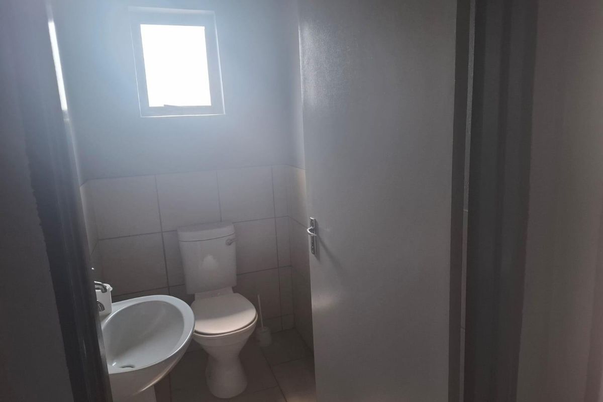 A functional bathroom featuring a pedestal basin, a standard toilet, and tiled wall finishes with natural light from a small window.