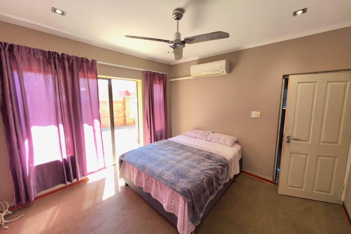 A bedroom featuring carpeted flooring, a ceiling fan, a wall-mounted air conditioning unit, and sliding glass doors providing access to the exterior.