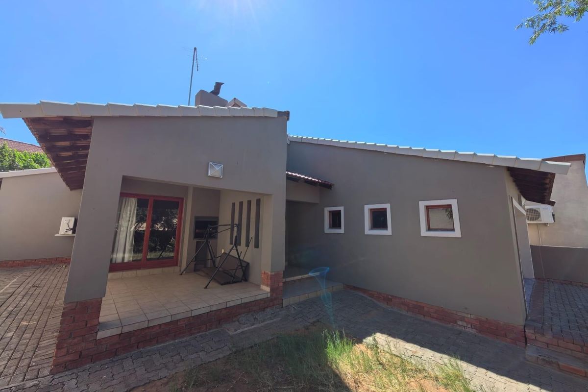 Rear view of the townhouse featuring a covered patio area with built-in braai, tiled flooring, and paved exterior surrounds.