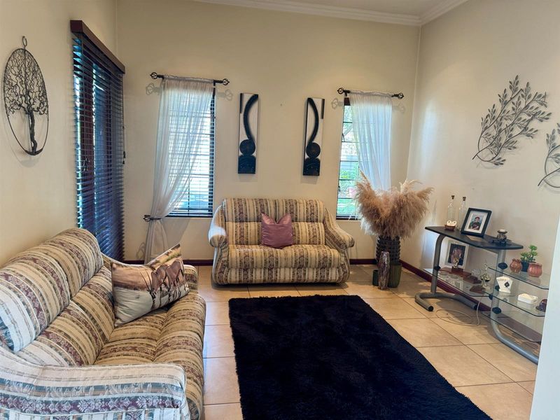 A comfortable living room featuring tiled flooring, neutral wall tones, and natural light provided by windows fitted with venetian blinds and curtain rods.