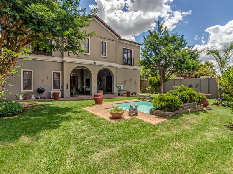 Rear view of a two-story house featuring a covered patio, a swimming pool, and a landscaped garden with mature trees.