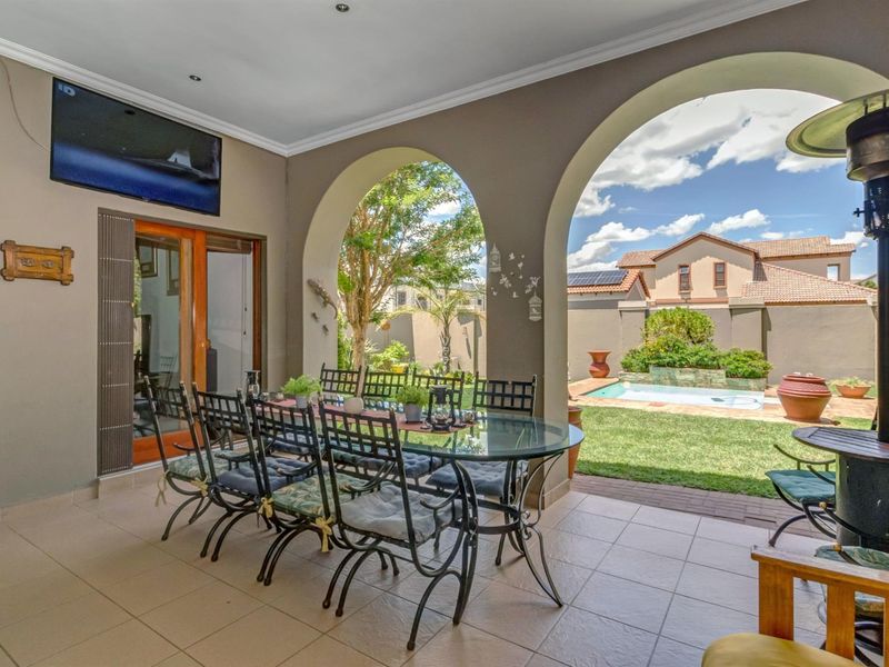 A spacious covered patio featuring tiled flooring and elegant arched openings, providing a seamless transition to the garden and pool area.