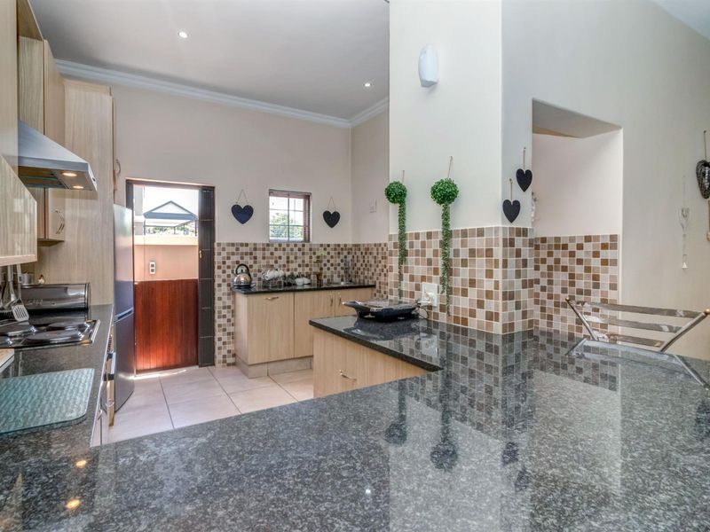 A functional kitchen featuring granite countertops, light wood cabinetry, a gas hob with extractor fan, and a tiled backsplash with direct outdoor access.