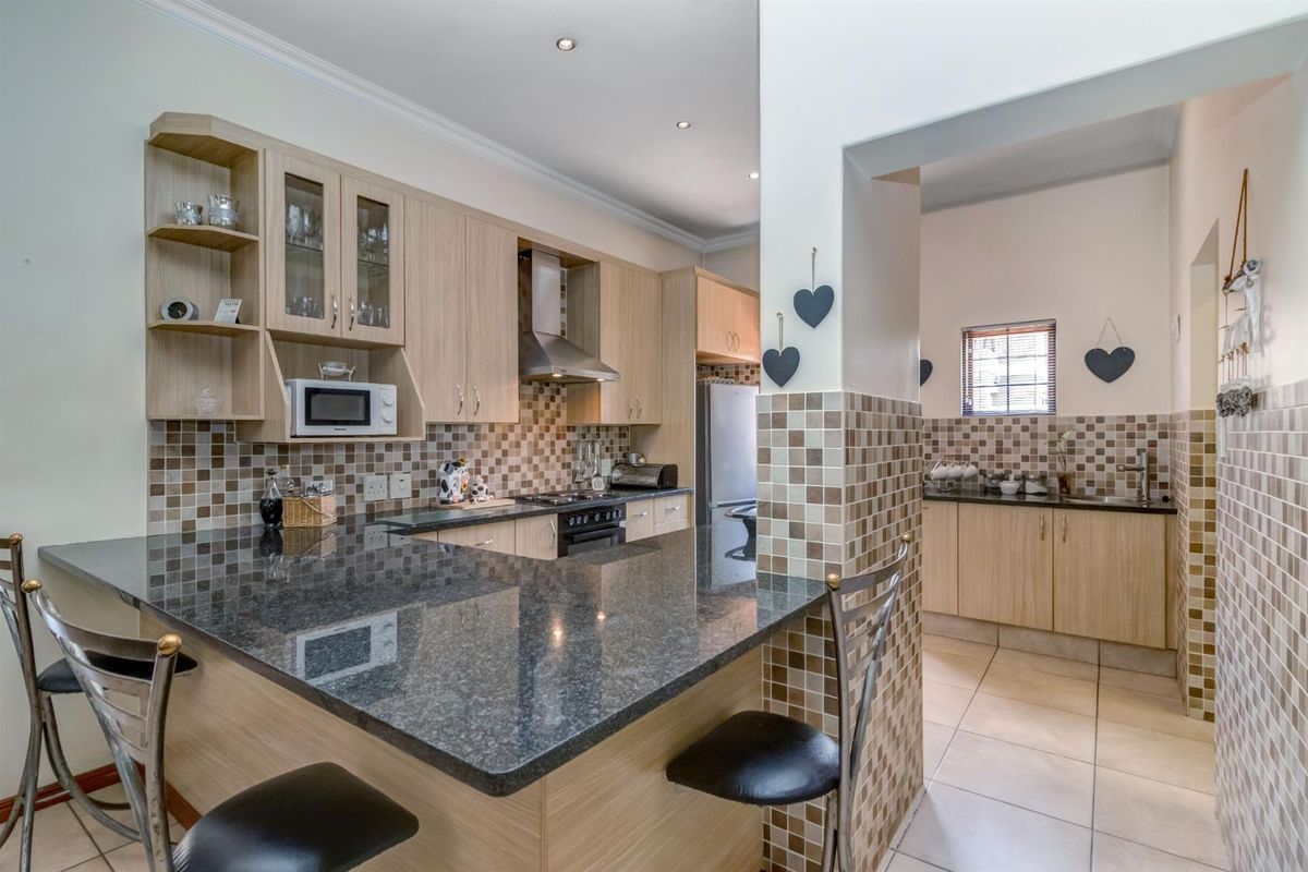 A functional kitchen featuring light wood cabinetry, granite countertops, a breakfast bar, and a separate scullery area with matching mosaic tile backsplashes.