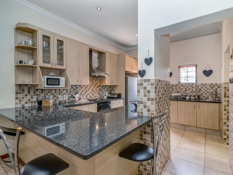 A functional kitchen featuring light wood cabinetry, granite countertops, a breakfast bar, and a separate scullery area with matching mosaic tile backsplashes.