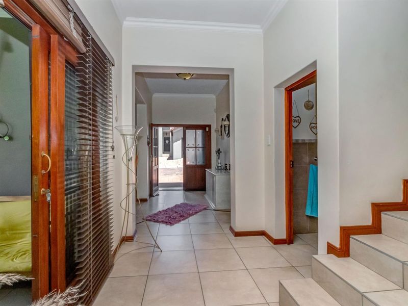 A bright, tiled hallway featuring timber door frames, a staircase, and a sliding door leading to an outdoor area.