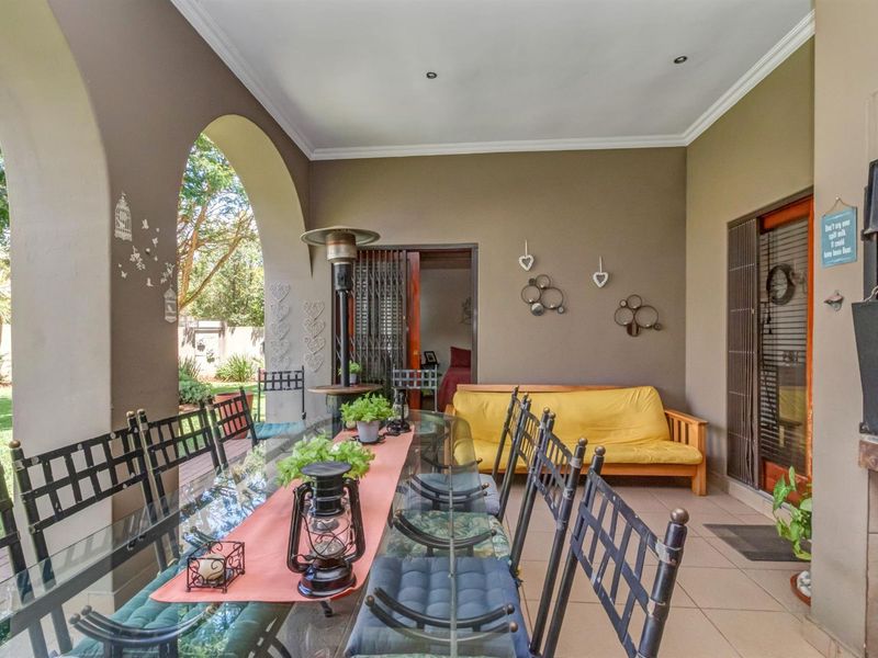 A spacious covered patio featuring tiled flooring, arched architectural details, and a built-in braai, perfect for outdoor dining and entertaining.