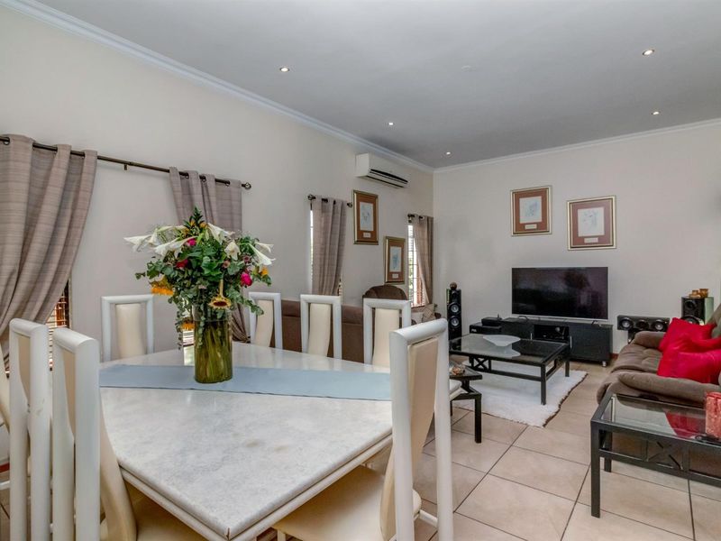 Spacious open-plan living and dining area featuring neutral tiled flooring, recessed downlighting, and a wall-mounted air conditioning unit.