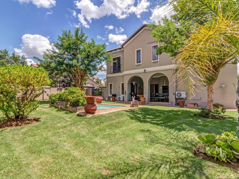 A well-maintained rear exterior view featuring a landscaped garden, a swimming pool, and a covered patio area attached to the two-story residence.