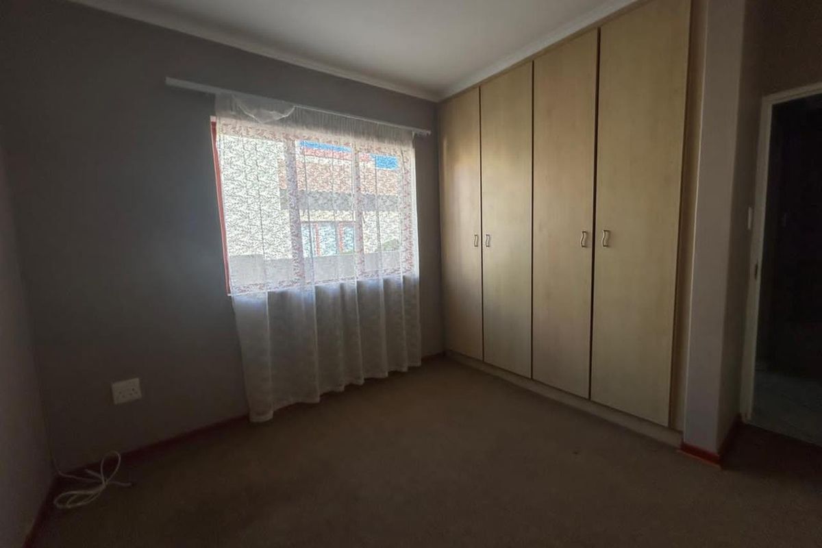 A bedroom featuring built-in wooden cupboards and carpeted flooring, providing a functional and neutral space.