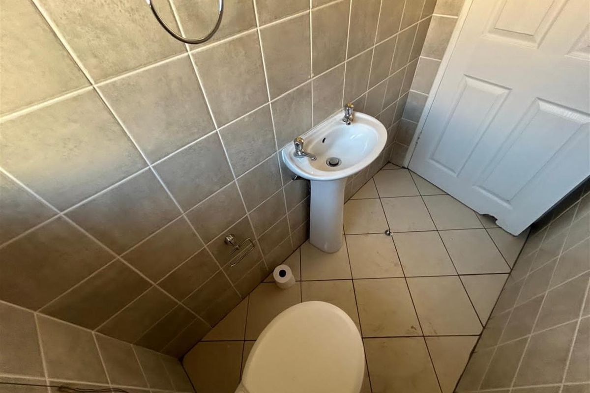 A compact guest bathroom featuring a pedestal sink, toilet, and neutral wall tiling with diagonal floor tiles.