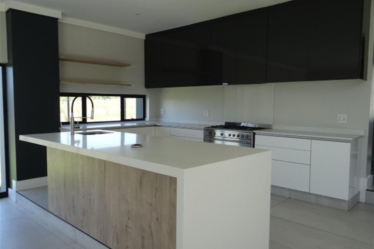 Modern kitchen featuring a central island with stone countertop, sleek black upper cabinetry, white lower cabinets, and a stainless steel gas stove.