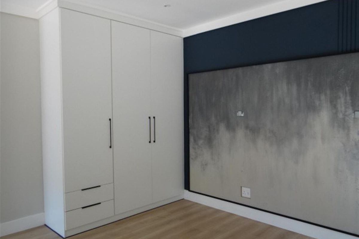 A modern bedroom featuring built-in white cabinetry with sleek handles and a decorative feature wall with integrated electrical outlets.