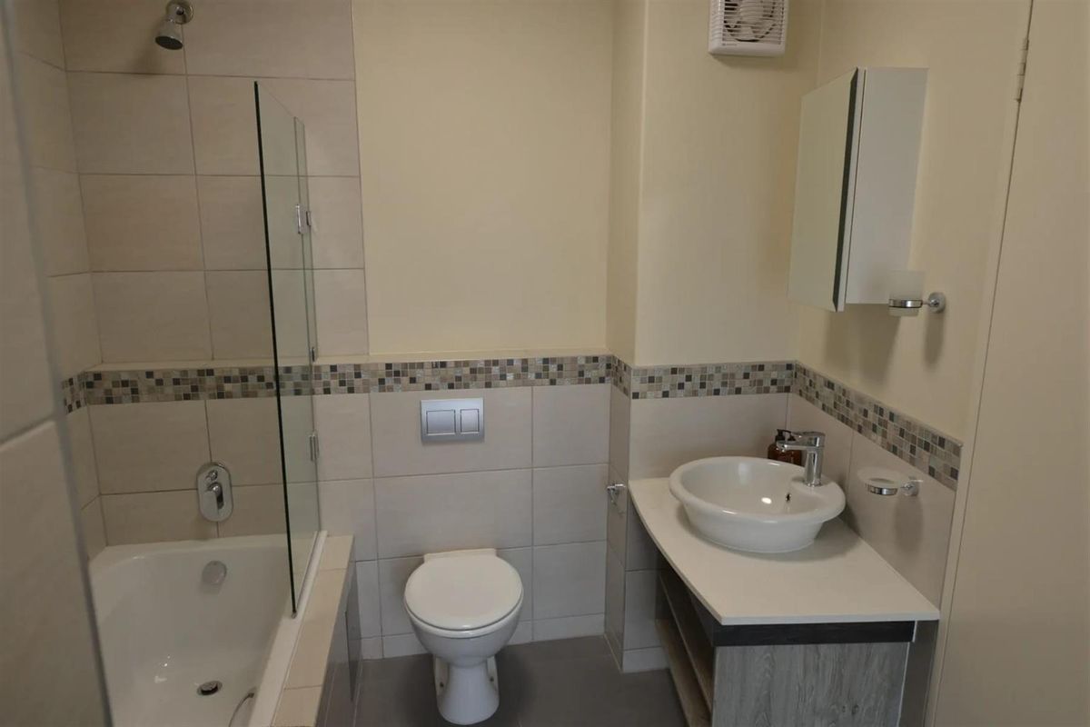 A modern bathroom featuring a shower-over-bath combination with a glass screen, a wall-mounted toilet, and a vanity basin with storage.