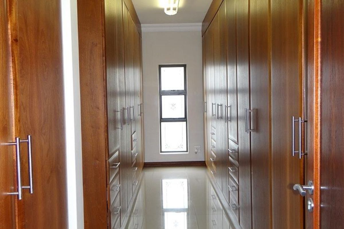 A well-maintained walk-in closet or dressing area featuring extensive floor-to-ceiling wooden cabinetry, tiled flooring, and a central window for natural light.