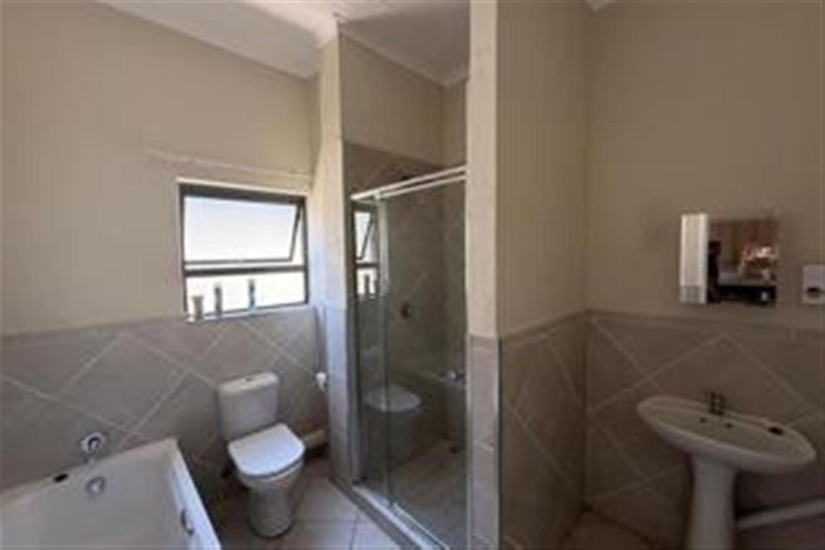 A functional bathroom featuring a bathtub, a separate glass-enclosed shower, a pedestal basin, and a toilet with neutral wall tiling.