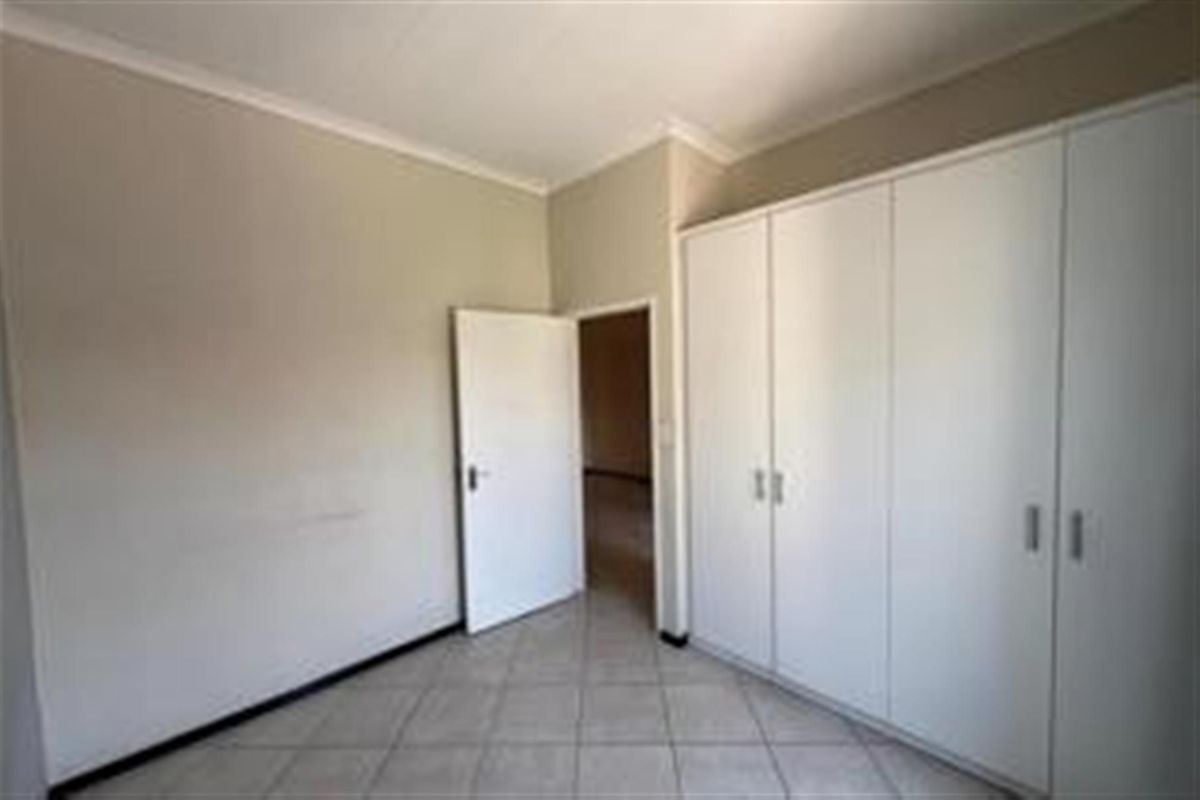 A bedroom featuring neutral wall tones, tiled flooring, and built-in white cabinetry providing ample storage space.
