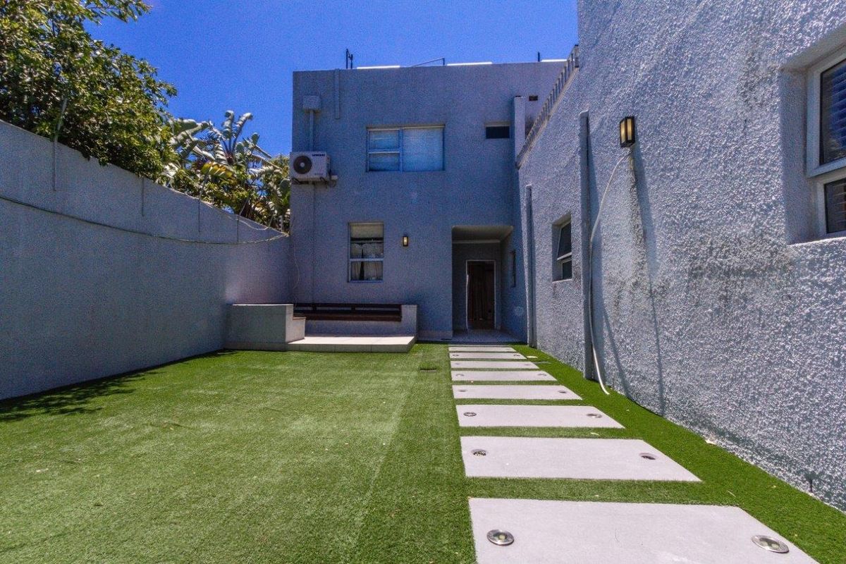 A private rear courtyard featuring artificial turf, concrete paver pathway, and a built-in bench seat against the boundary wall.