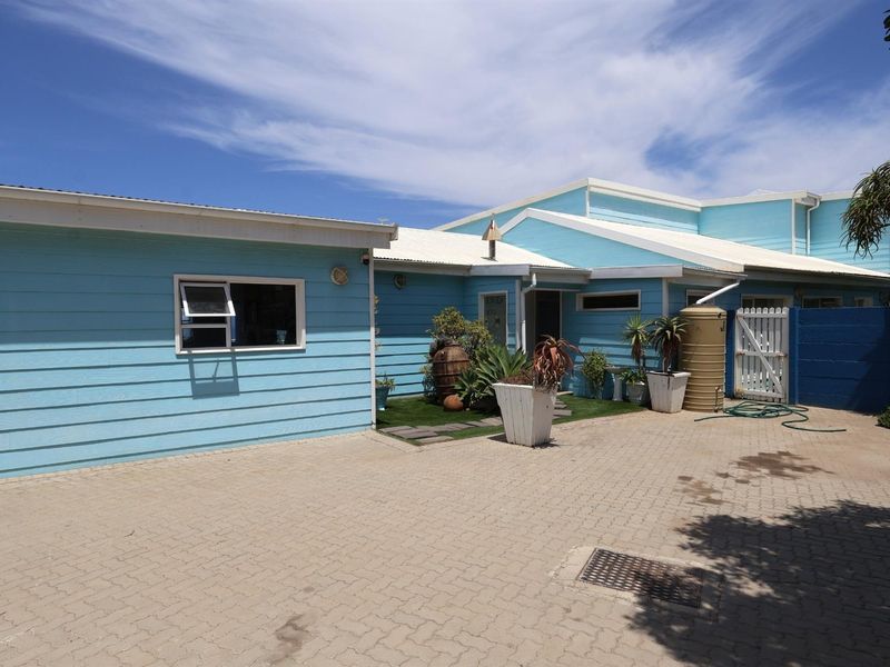 A view of the front exterior featuring light blue timber-style cladding, paved driveway, and a water storage tank.