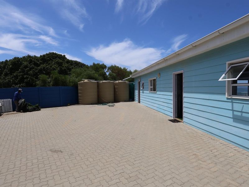 Exterior view of the property featuring a paved driveway, light blue timber-style siding, and multiple water storage tanks located at the rear.