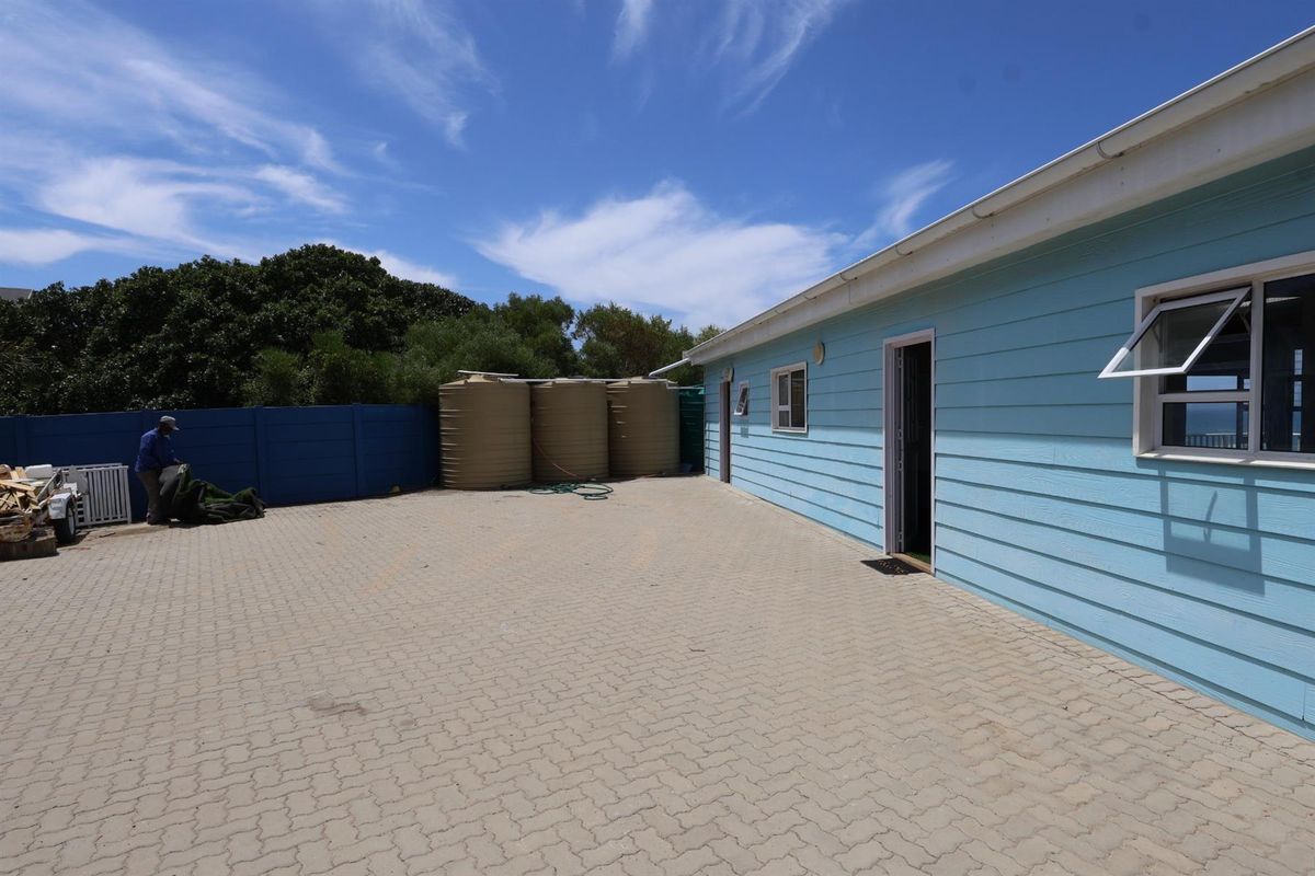 Exterior view of the property featuring a paved driveway, light blue timber-style siding, and multiple water storage tanks located at the rear.