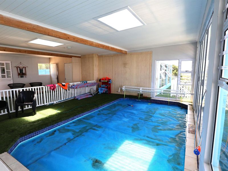 Indoor swimming pool area featuring a tiled surround, artificial turf flooring, skylights, and large glass sliding doors providing natural light.