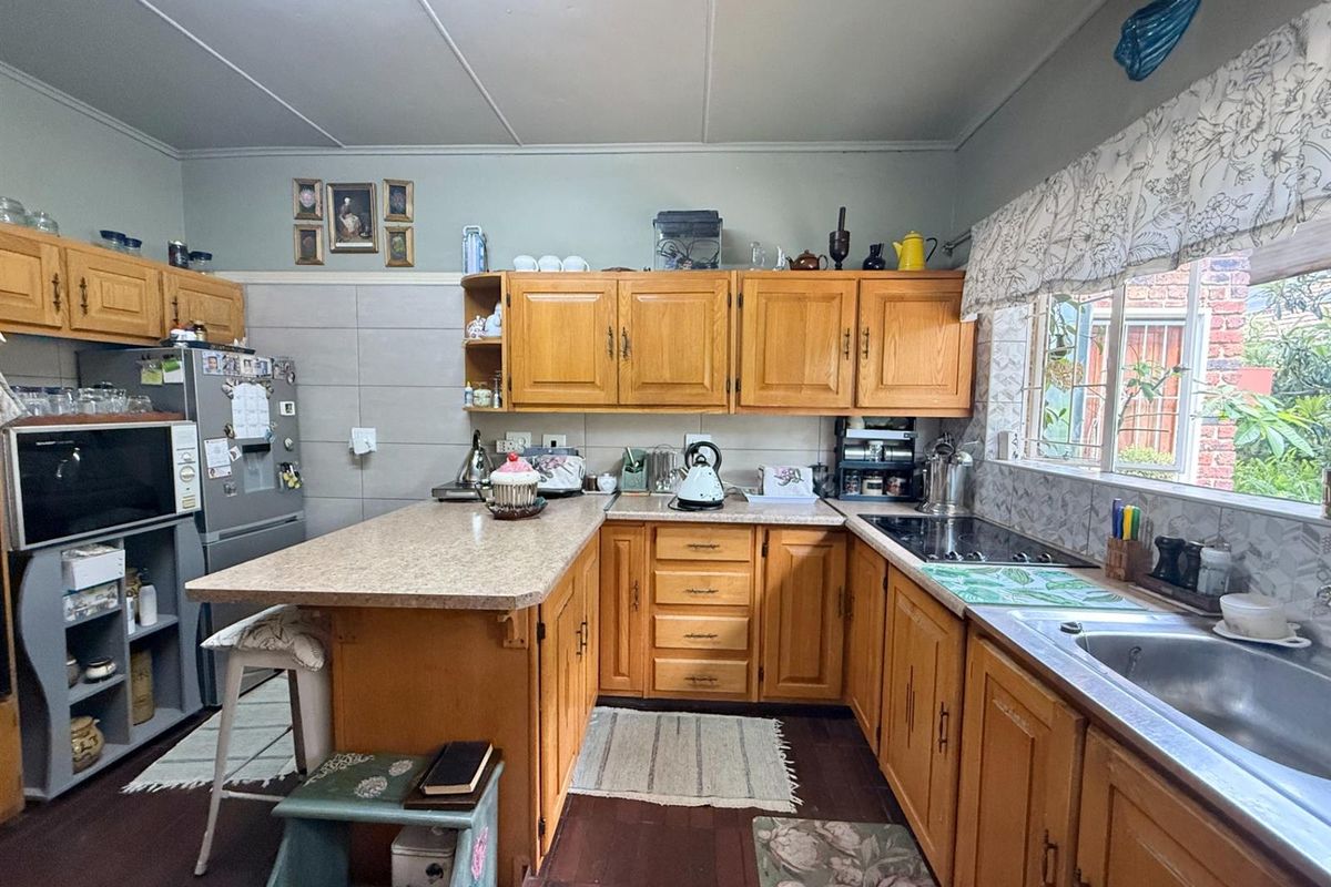 A functional kitchen featuring traditional timber cabinetry, laminate countertops, a built-in hob, and a stainless steel sink with a window view.