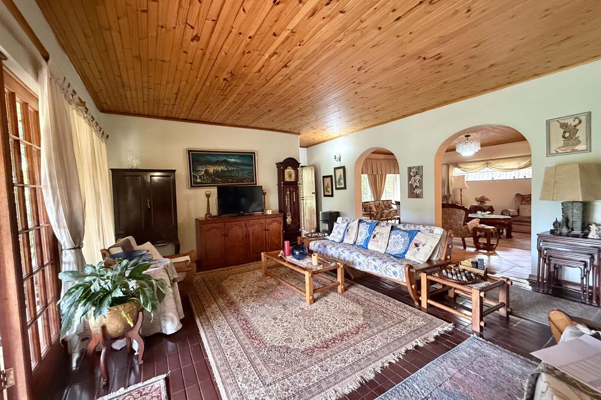 Spacious living room featuring a distinctive timber-clad ceiling, tiled flooring, and arched doorways leading to an adjoining living area.
