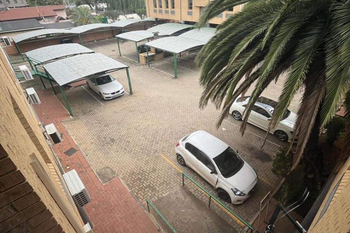 Elevated view of a commercial parking area featuring multiple covered parking bays, paved surfaces, and surrounding brick building facades.