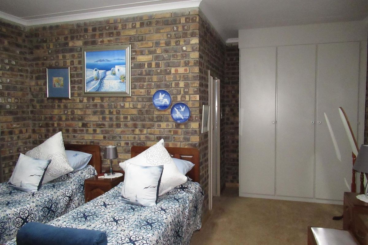 A bedroom featuring a rustic face-brick feature wall and built-in floor-to-ceiling cupboards with neutral carpeting.
