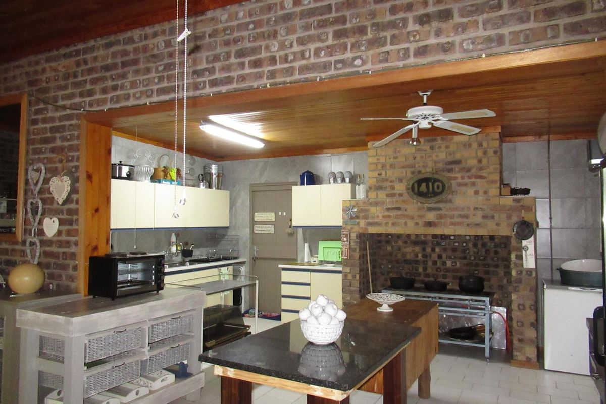 Rustic farmhouse kitchen featuring exposed brick walls, timber ceiling, built-in brick fireplace, and functional cabinetry with tiled flooring.