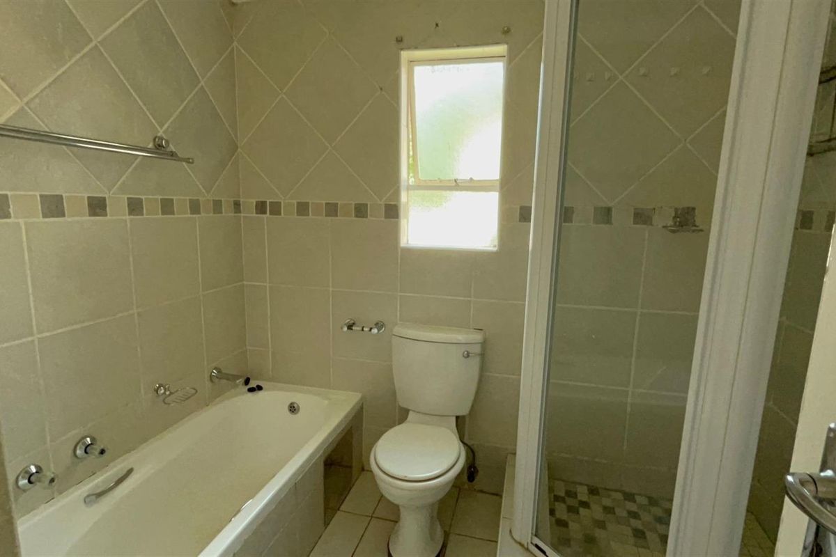 A functional bathroom featuring a built-in bathtub, separate shower enclosure, and toilet, finished with neutral ceramic wall and floor tiling.