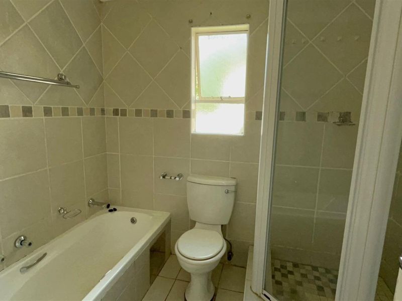 A functional bathroom featuring a built-in bathtub, separate shower enclosure, and toilet, finished with neutral ceramic wall and floor tiling.