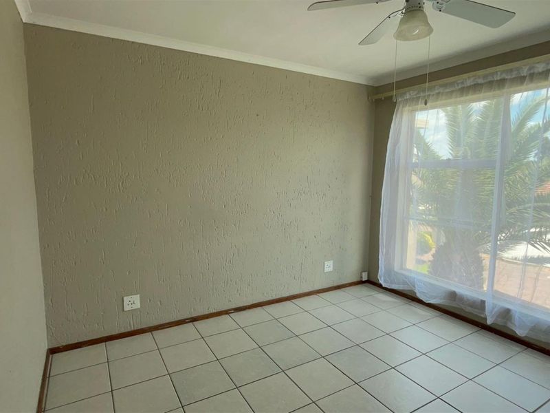 An empty bedroom featuring tiled flooring, a ceiling fan, and a large window with natural light, ready for personalization.