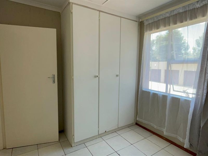 A functional bedroom featuring built-in cupboards and tiled flooring, offering a clean and neutral space ready for personalization.