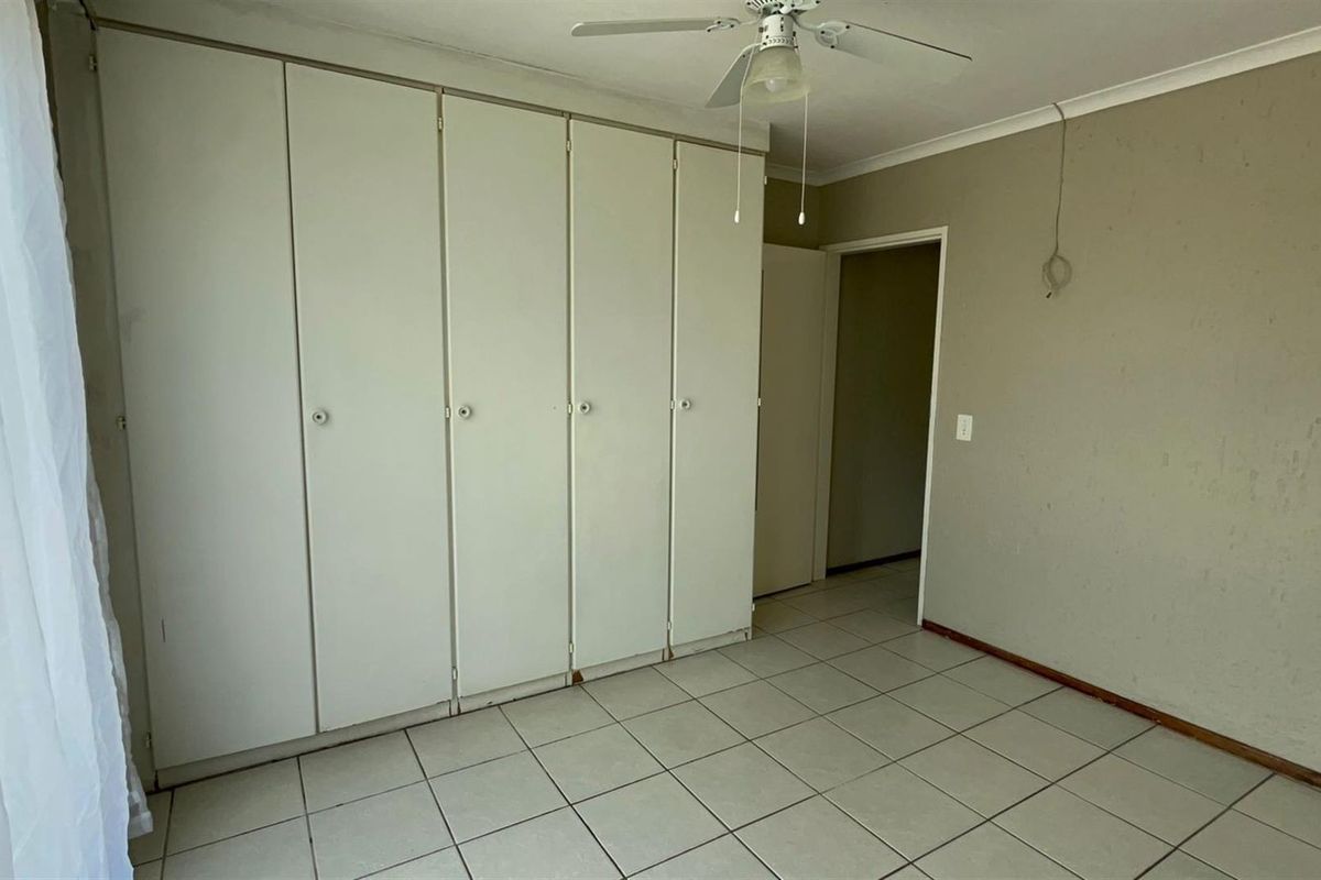 An empty bedroom featuring built-in cupboards, tiled flooring, and a ceiling fan, requiring minor cosmetic updates to the walls and electrical fixtures.