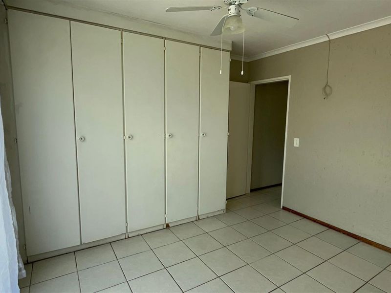 An empty bedroom featuring built-in cupboards, tiled flooring, and a ceiling fan, requiring minor cosmetic updates to the walls and electrical fixtures.