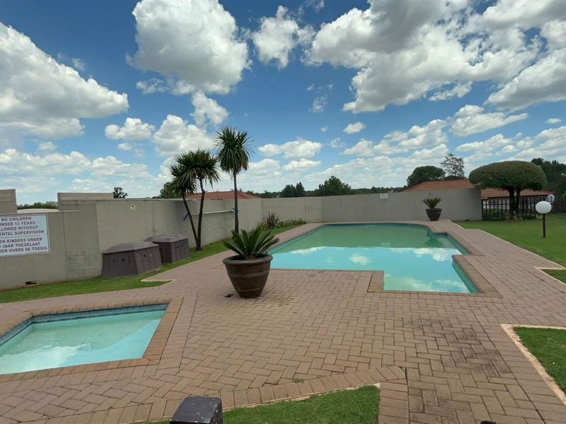 Communal swimming pool area featuring a paved deck, boundary walls, and landscaped lawn, suitable for outdoor recreation within the townhouse complex.