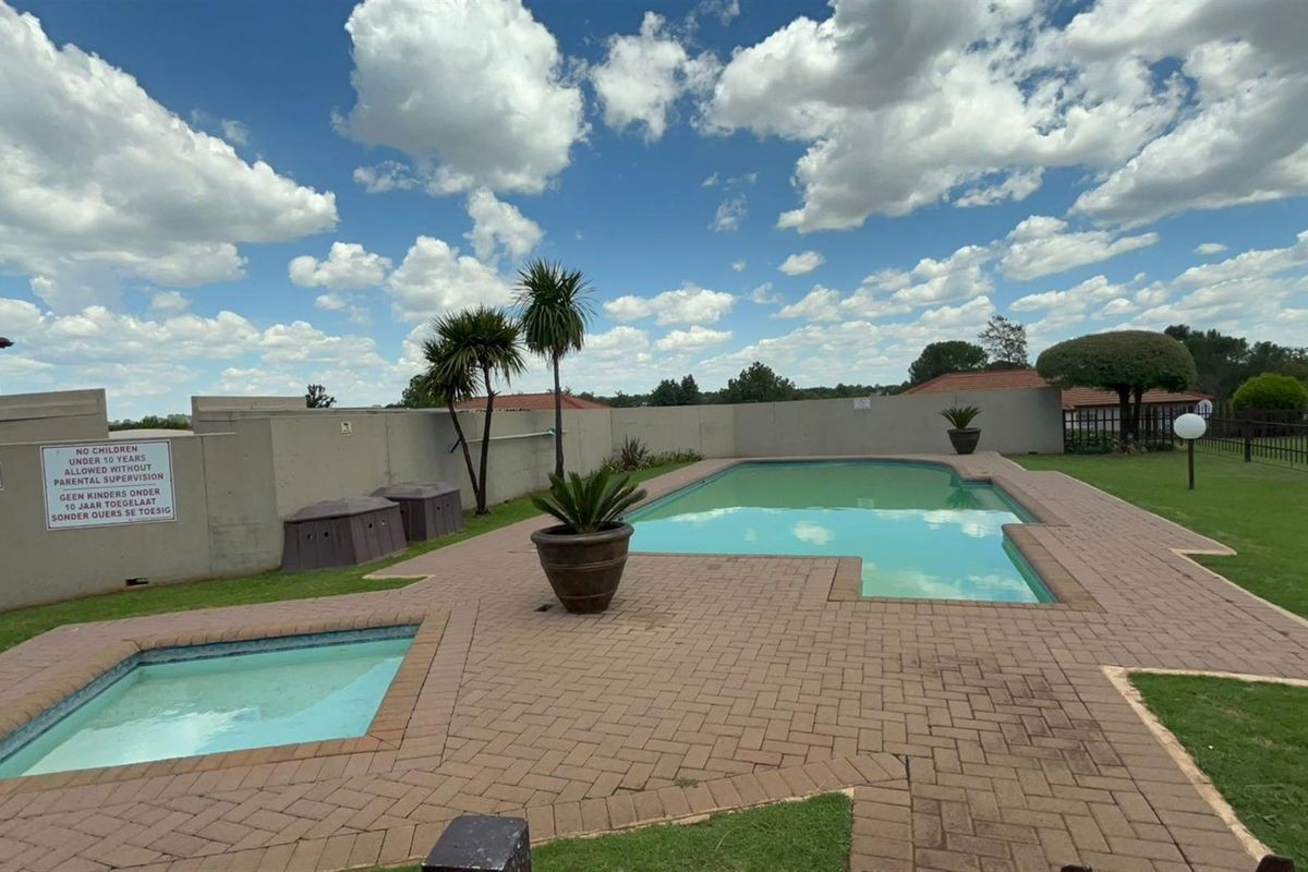 Communal swimming pool area featuring a paved deck, boundary walls, and landscaped lawn, suitable for outdoor recreation within the townhouse complex.