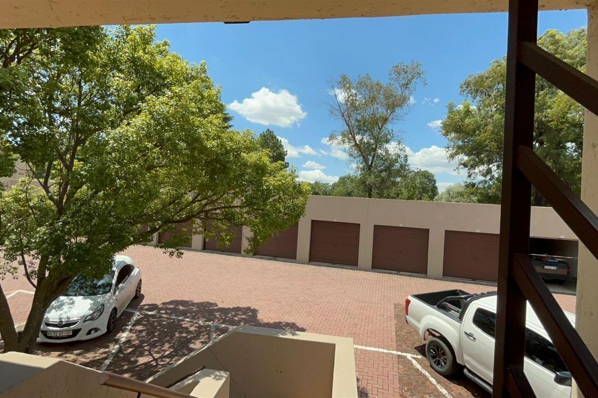 View from an elevated balcony overlooking a paved communal driveway and a row of residential garage doors.