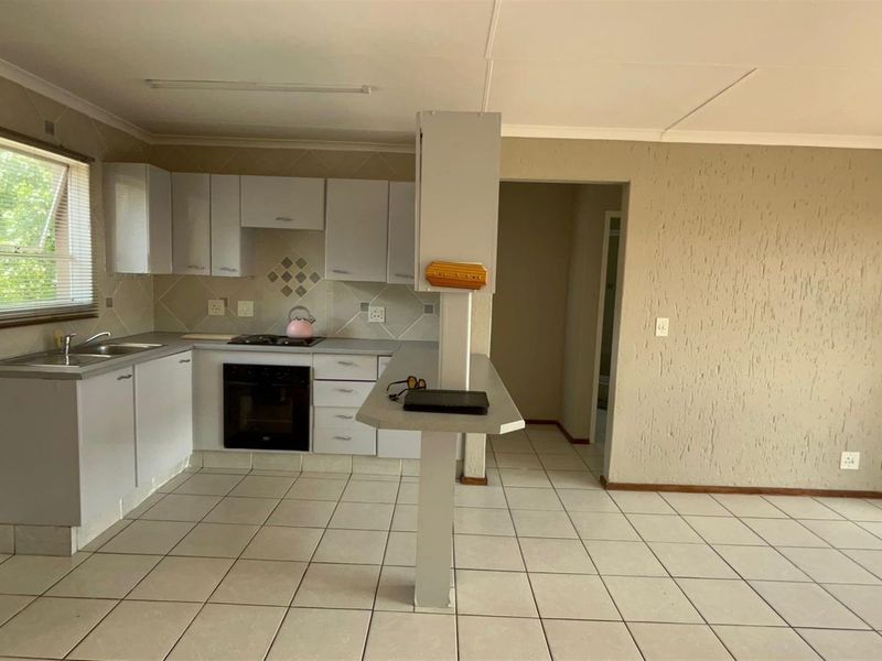 Open-plan kitchen area featuring built-in cabinetry, oven, hob, and a breakfast bar, with tiled flooring throughout the space.