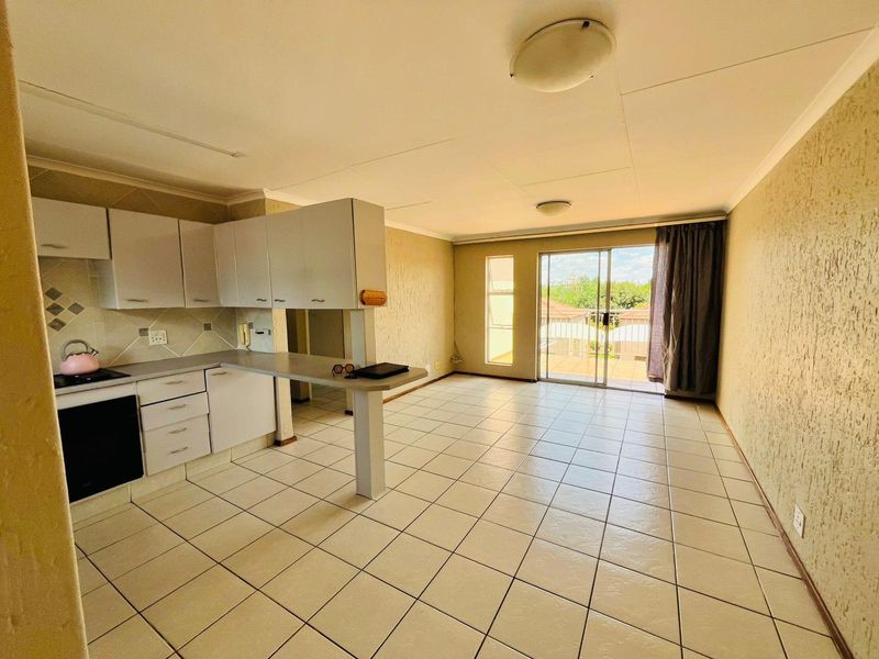 Open-plan living area featuring a functional kitchen with built-in cabinetry, tiled flooring, and direct access to a balcony through a sliding glass door.