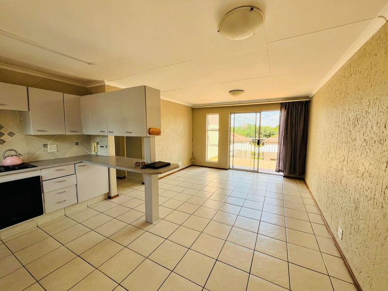 Open-plan living area featuring a functional kitchen with breakfast bar, tiled flooring, and sliding door access to a balcony.