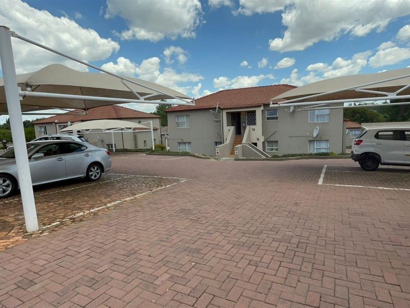 Front exterior view of a townhouse complex featuring paved parking areas with shade cloth carports and a multi-level residential building.