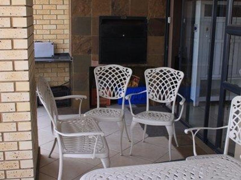 Covered patio area featuring a built-in braai, stone wall cladding, and tiled flooring, providing a functional outdoor entertainment space.