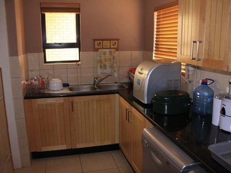A functional scullery area featuring timber cabinetry, granite countertops, a double stainless steel sink, and tiled splashbacks with natural light from two windows.