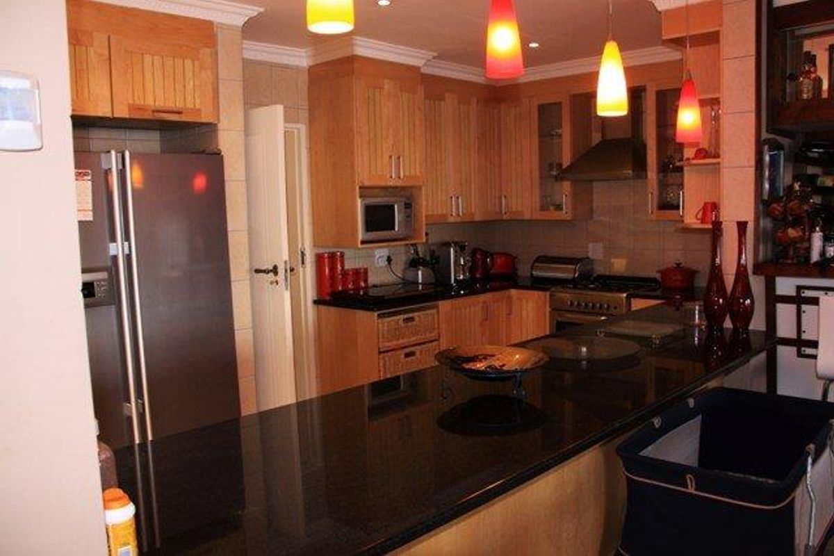 A functional kitchen featuring wooden cabinetry, granite countertops, built-in appliances, and a breakfast bar, illuminated by modern pendant lighting.