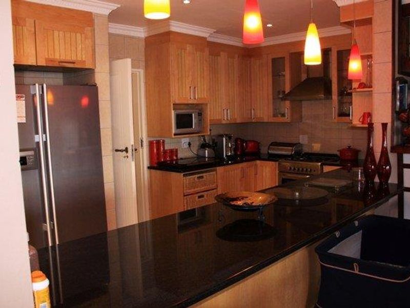 A functional kitchen featuring wooden cabinetry, granite countertops, built-in appliances, and a breakfast bar, illuminated by modern pendant lighting.