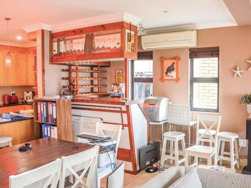 Open-plan living area featuring a built-in wooden bar with integrated wine storage, adjacent kitchen cabinetry, and a wall-mounted air conditioning unit.