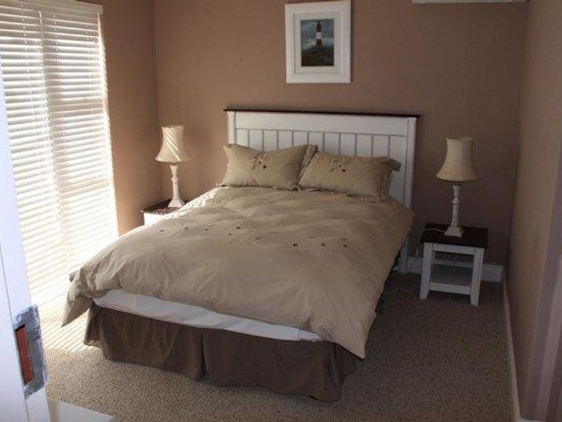 A cozy bedroom featuring neutral wall tones, carpeted flooring, and venetian blinds allowing natural light into the space.